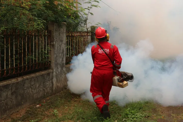 Técnico uniformizado aplicando termonebulização ao redor de um imóvel
