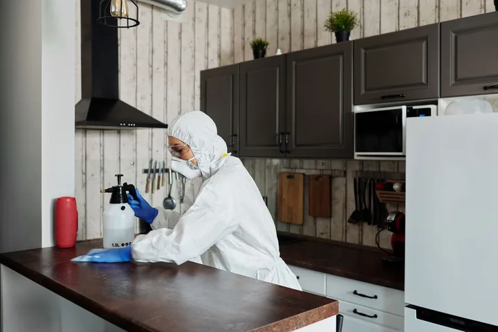 Profissional de EPI desinfetando a bancada de uma cozinha