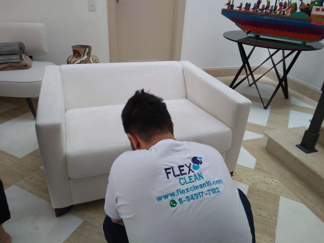Técnico da Flex Clean passando a extratora no assento de um sofá claro de dois lugares, na sala do cliente