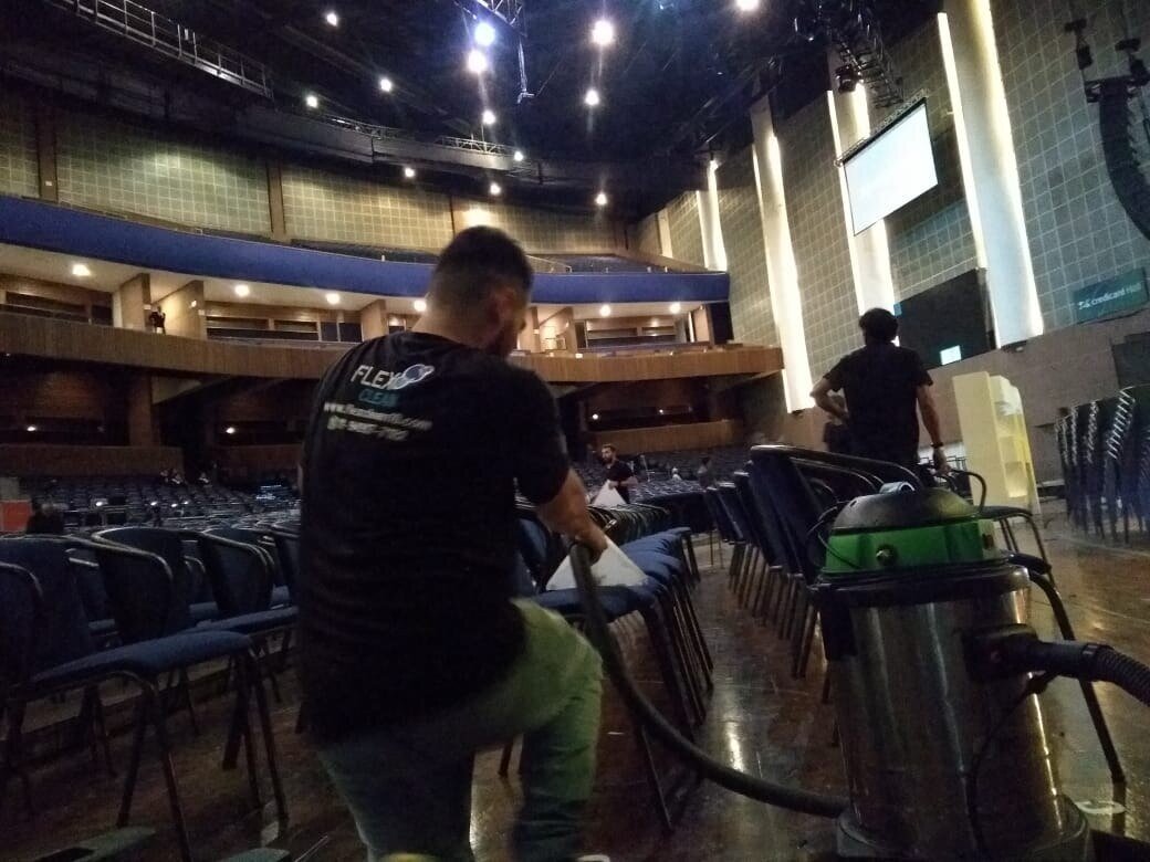 Técnico higienizando fileiras de cadeiras estofadas de um auditório com uma extratora profissional