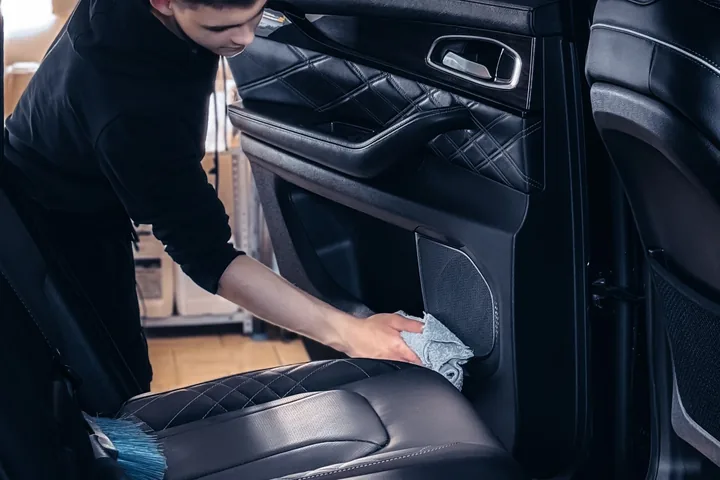 Profissional tratando o banco de um veículo com produto e pano, dentro do carro