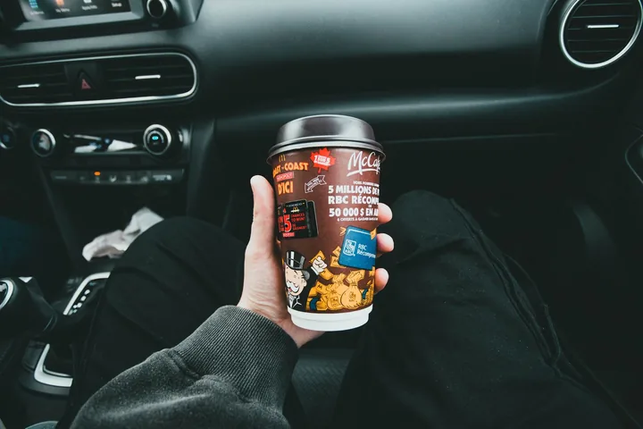 Copo de café aberto sendo segurado dentro de um carro, sobre o banco