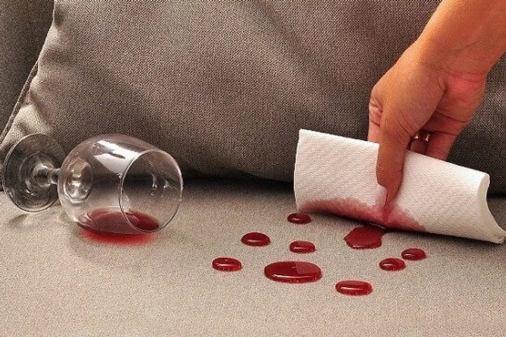 Taça de vinho tinto caída sobre o assento de um sofá claro, com papel absorvendo o líquido