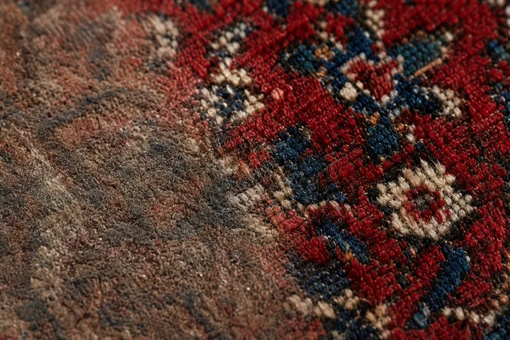 Close da trama de um tapete persa: metade apagada pela sujeira e metade com as cores vivas